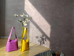 Fashionable handbags of bright colors on a shop window against the background of a bouquet and...