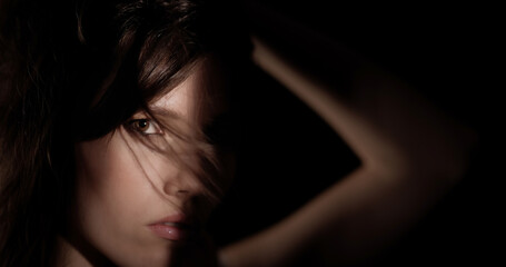 Close up portrait of mysterious young woman with brown hair covering part of her face with arm in...