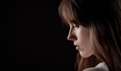 Fototapeta premium Profile of a beautiful young woman with long brown hair looking down, isolated on a black background