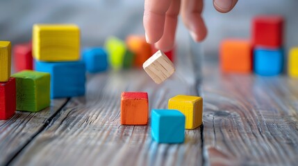 A hand placing a wooden block onto a wooden surface with colorful blocks scattered around.