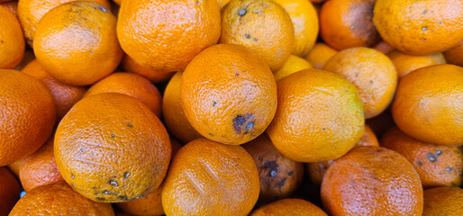 Stack of ripe oranges with rough, dimpled skin, showing natural spots and minor blemishes, captured in bright daylight. oranges; fruit;