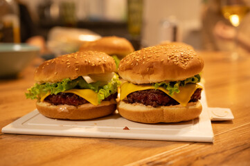 Freshly made hamburgers with melted cheese, lettuce, tomato, and sauce, sitting on a white cutting...