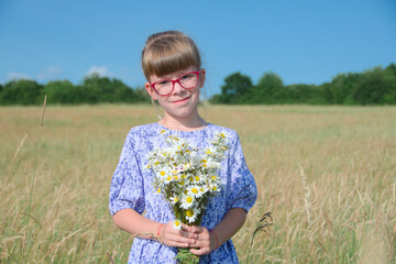 girl with glasses in a dress stands in a field with a bouquet of daisies on a bright sunny summer...
