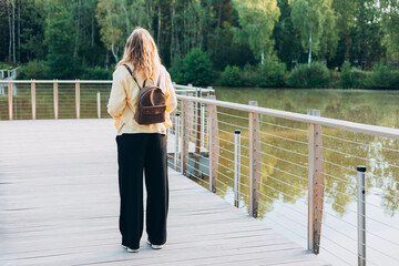 A young happy blonde woman standing on a bridge near a lake on a sunny day. Beautiful morning relax, Full body