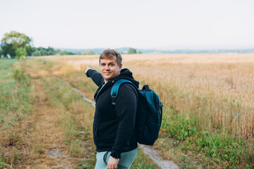One Caucasian male hiking in the woods in summer. Travel, active lifestyle, people and hobby concept. Blonde happy man in sport clothes pointing finger outdoors. Traveler enjoys eco-tourism, rear view