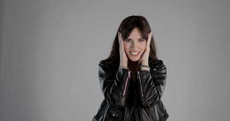 Studio portrait of cheerful stylish rocker covering ears with hands and smiling on gray background
