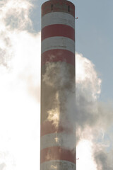 A tall, red and white striped chimney is billowing smoke out of its top, contributing to the...