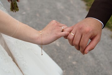 Wedding Hands Holding Intertwined with Gold Rings, White Dress, Romance, Commitment, Love, Marriage, Celebration, Outdoor Ceremony, Couple, Brown Coat