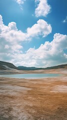 Serene landscape of a dry lake bed with cracked earth, surrounded by distant mountains under a vibrant blue sky with fluffy white clouds