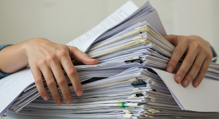 Person holding a large stack of paper documents with hands in an office setting