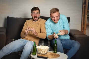 Happy friends playing video games with joystick sitting on sofa