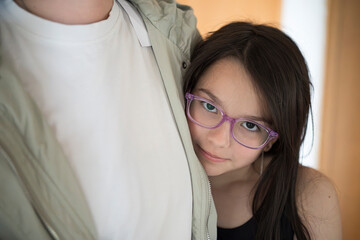 Sweet girl in glasses hugging her mom (or parent) indoors. Concept: family love, warmth, close bond, comfort, emotional connection.