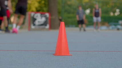 The scene shows bright orange cones used for basketball drills on a court with players engaged in training and gameplay, focusing on skill development, teamwork, and competition - Powered by Adobe