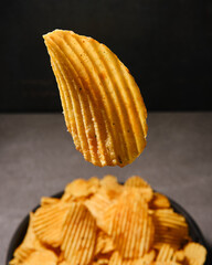 Wavy potato chips close-up on a background of a bowl of chips in defocus. Snacks for a party....