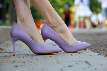 Stiletto heels, female legs in purple high-heeled shoes close up. Slim woman on the city street in...