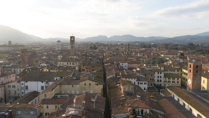 View from Torre delle Ore of Via Fillungo in Lucca, Italy, showing rooftops, medieval towers and Tuscan hills in soft afternoon light.