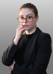 Une jeune femme dans l'expectative avec des lunettes pose dans un costume noir sur un fond gris...