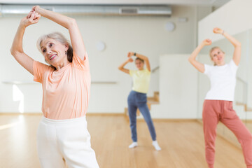 Portrait of cheerful active female pensioner exercising dance moves in fitness studio