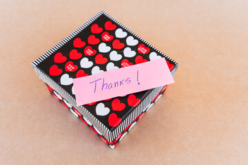 Thank you note that says thank you handwritten with blue pen with a background of a gift box with...