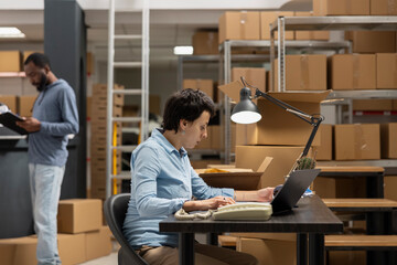 Woman focused employee uses laptop to check logistics for order processing, working in a local...