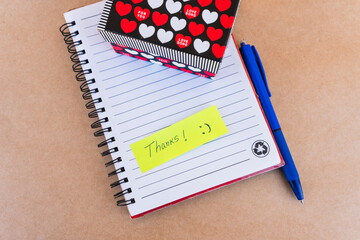 Thank you note that says thank you handwritten with blue pen with a gift box with red and white...