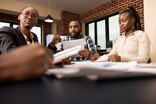 Black colleagues work together at conference table, reviewing financial paperwork and sharing insights during productive business discussion. African american male and female employees in a meeting.