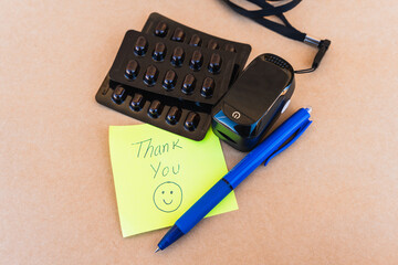 Thank you note that says thank you handwritten with blue pen with a background of an oximeter and...