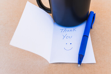 Thank you note that says thank you handwritten with blue pen with a coffee cup background