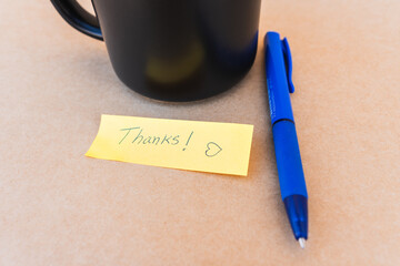 Thank you note that says thank you handwritten with blue pen with a coffee cup background