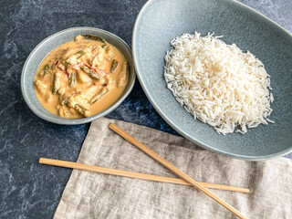 red Thai chicken Curry dish. sauce in bowl. rice in separate plate in pastel blue plate with chopsticks on napkin high angle view, close up
