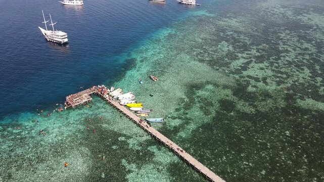 Aerial drone view of Kanawa Island beach with long bridge dock and sailing boats around.