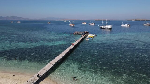 Aerial drone view of Kanawa Island beach with long bridge dock and sailing boats around.