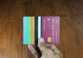 The right hand holds several dummy credit cards on a wooden patterned table.
