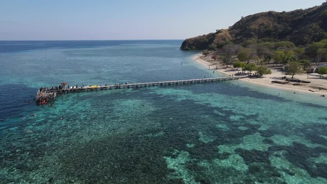 Aerial drone view of Kanawa Island beach with long bridge dock and sailing boats around.