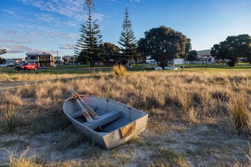 A small aluminum boat with oars rests on the sandy shore of Whangamata, Coromandel Peninsula, New...