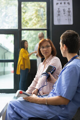 Asian woman does health check with nurse monitoring blood pressure with electronic device, checking...