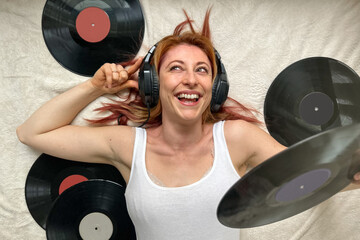 Ginger-haired woman, 30s, lying on bed in cozy home wear, listening to music with headphones....