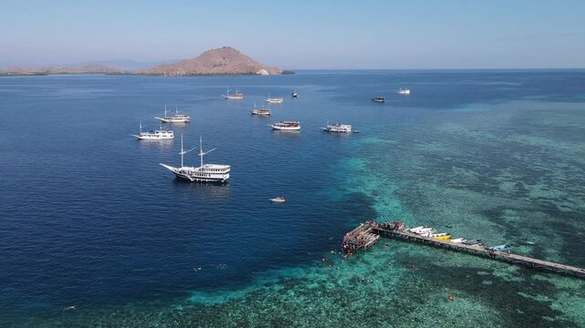 Aerial drone view of Kanawa Island beach with long bridge dock and sailing boats around.