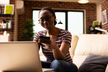 African american woman enters bank card details on laptop while making digital payment at home....