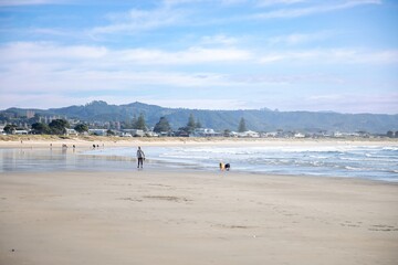 People and dogs enjoy a sunny day at Whangamata, Coromandel Peninsula, New Zealand. The beach is a popular spot for recreation and relaxation.