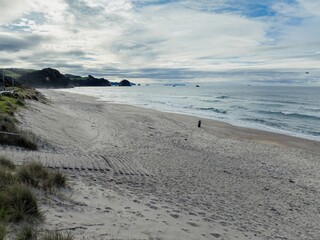 A lone person walks along the sandy beach of Whiritoa, Coromandel Peninsula, New Zealand, enjoying...
