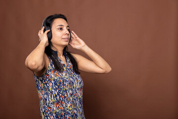Indian female individual looking sideways, touching her headphones and listening intently to a...