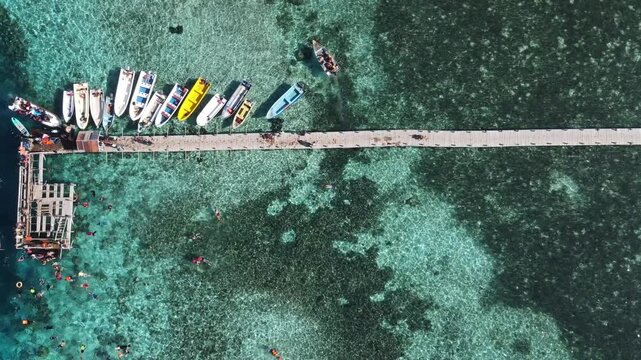 Aerial drone view of Kanawa Island beach with long bridge dock and sailing boats around.