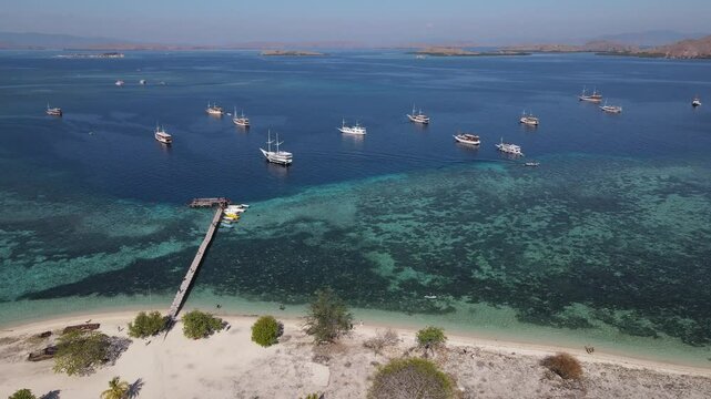 Aerial drone view of Kanawa Island beach with long bridge dock and sailing boats around.