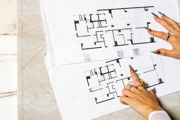 Architect with long nails reviewing blueprints on table for building project