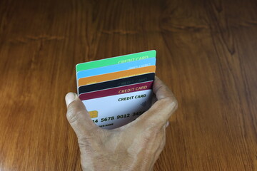 The right hand holds several dummy credit cards on a wooden patterned table.