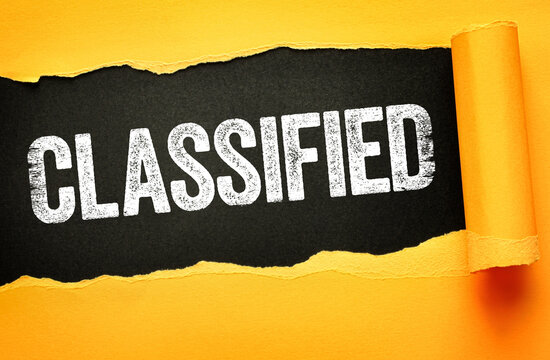 CLASSIFIED in bold white distressed font on a black background revealed through torn yellow paper. Secrecy, confidentiality, private or top-secret information visual concept