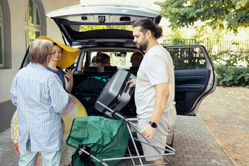 In the driveway, a big family loading their packed car with baggage and folding chair....