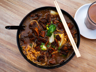 Large portion of noodle soup with beef, complemented with chopped greens, is served in deep bowl. Chopsticks or spoon are served with dish on request