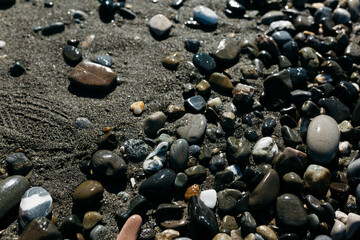 glossy stones washed by the sea wave shine from the rays of the sun on a summer day. pebbles on the city beach.the concept of environmental protection from pollution by petroleum products and plastics